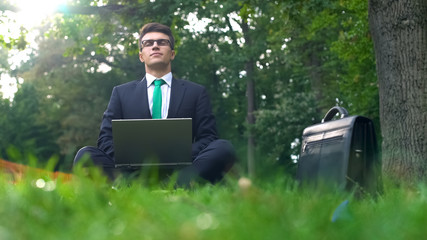 Young manager working on laptop in forest, enjoying nature, escape from office