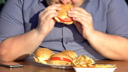 Obese hungry man eating fatty burgers, unhealthy food addiction, overweight