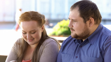 Fototapeta premium Shy fat couple sitting in outdoor cafe during romantic date, awkward situation