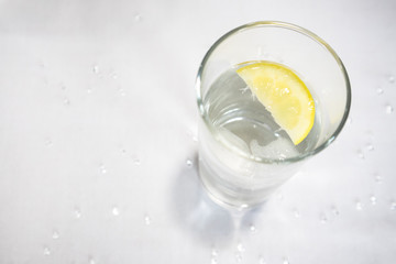 Clear glass with water, ice and lemon slices on white background with glitter