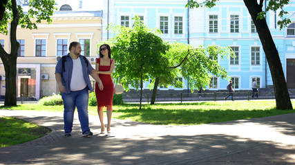 Fototapeta na wymiar Beautiful woman and fat man holding hands walking in park, dream, leisure time