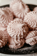 Pink homemade marshmallow (zephyr) on a black plate with sugar powder