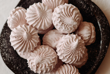Pink homemade marshmallow (zephyr) on a black plate with sugar powder