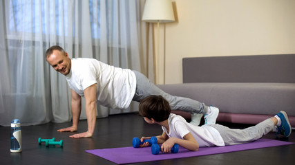 Serious sportive family doing plank exercise with dumbbells at home, role model