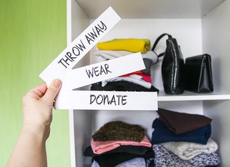 Clothes sorting in home wardrobe for donation, wearing and discard. Wear, Donate and Throw away paper notes in a hand on white shelf background.