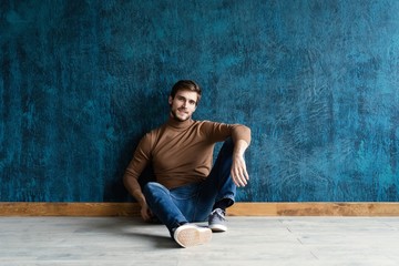 young casual fashion man sitting on the floor isolated on dark blue background.