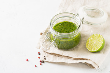 Green sauce chimichurri with fresh herb and spices in jar on white background
