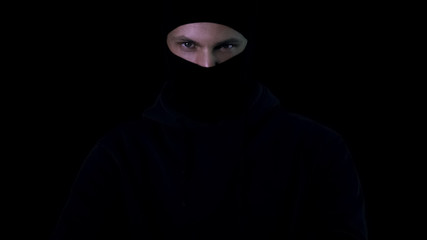 Dangerous male in balaclava looking in camera on black background, terrorism