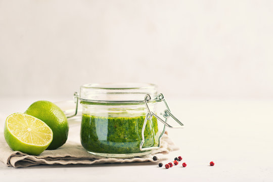 Green sauce chimichurri with fresh herb and spices in jar on white background