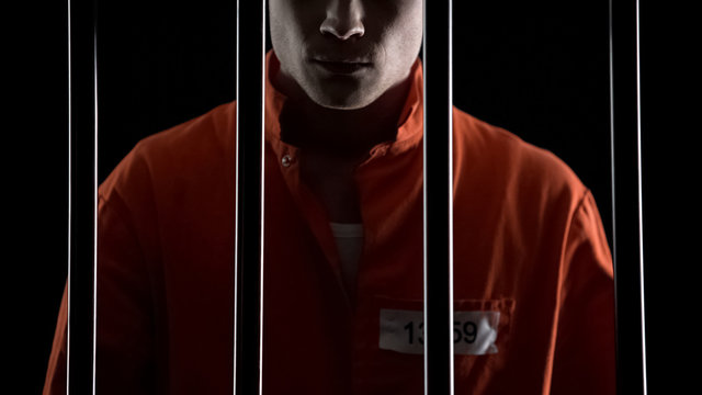 Criminal in orange uniform behind prison bars, serving life sentence for murder