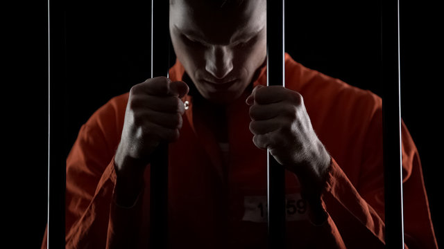 Thief in jail feeling sincere regret of crime, holding prison bars in desperate