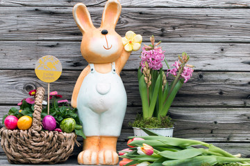 Fröhlicher Osterhase vor Holz mit Tulpen und Hyazinthen