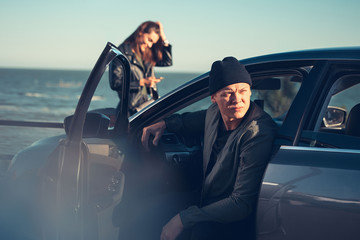 Young couple in love walks by the sea. Spring, autumn. The guy is wearing a jacket and hat. Girl in a hat and leather jacket with a scarf