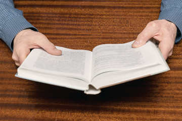 Naklejka premium open book in the hands of an old man at the table