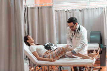 Female patient in pajamas lying down in hospital bed while doctor in white uniform folding her...