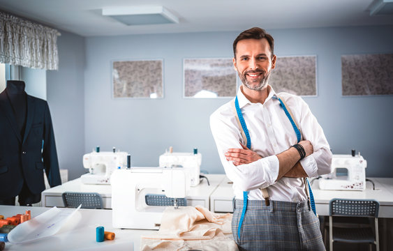 Smiling tailor shop owner standing above workshop desk, fashion design business