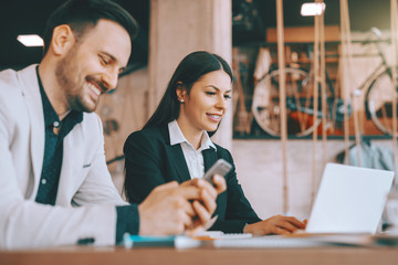 Two colleagues sitting in cafeteria and working on project. Man using smart phone while woman using laptop. Selective focus on woman. First learn, then remove L.