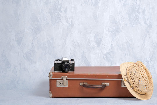 Travel carry on baggage, old fashioned suitcase, straw hat, film camera on grey background. Concept of travel with carry on luggage, elegant travel, journey.