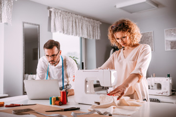 Obraz premium Professional tailors during work on project using laptop and sewing machine at fashion design studio