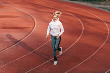 Fototapeta premium Caucasian female runner in sportswear running on the stadium with earphones in ears.