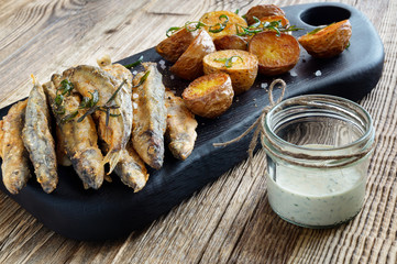 fish and chips decorated with fried rosemary and served with tartar sauce on wooden board