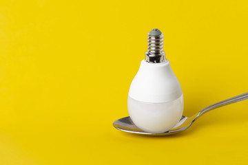 Light bulb on a spoon, on a contrasting yellow background. Minimalism creative concept