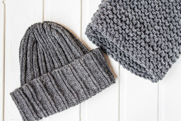 Grey knitted hat and scarf on the white wooden background