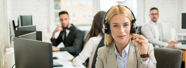 Portrait of beautiful female customer support operator with headset in call center