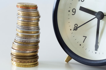 A pile of coins on the background of an alarm clock