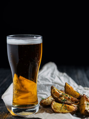 Glass of beer and country style potatoes with dill on dark background
