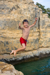 Boy jumping to the lake. Child jumping off a cliff into the sea. Summer fun