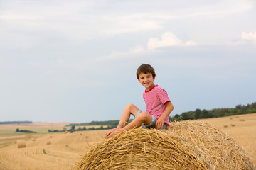 Naklejka na ściany i meble Cute preschool boy, sitting on hastack in field on a cloudy day