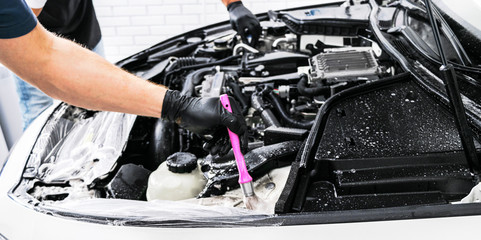 A man cleaning car engine with shampoo and brush. Car detailing or valeting concept. Selective focus. Car detailing. Cleaning with sponge. Worker cleaning. Car wash concept solution to clean