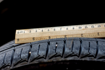 Close up wood ruler measure the tread of black tire