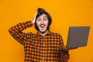 Photo of joyous guy 20s wearing plaid shirt holding and using silver laptop while standing isolated