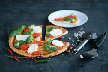 Sliced pizza with Mozzarella cheese, tomatoes, broccoli, Spices and fresh basil on black stone background. Italian pizza. One peece of pizza on a plate