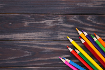 Many different colored pencils on a brown wooden background