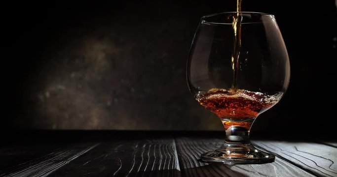Cognac is poured into a glass. On dark background. 4k.