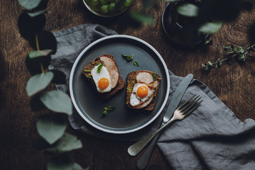 Ham and Fried Quail Egg Toast with Mustard and Basil on a dark wooden background, top view 