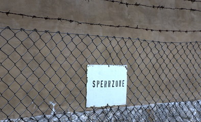Gefängnismauer mit Stacheldrahtzaun und Sperrzonen-Schild im Vordergrund