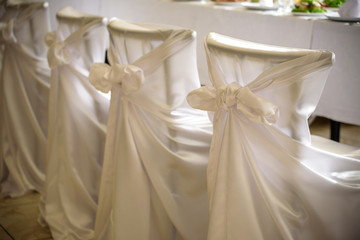 Decorated chairs with black fabric and big pink satin bows. Silk bow tied on back of chair in party at restaurant. Dark cloth cover chairs standing in a row