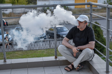 Elderly man hold and smoke his electronic cigarette outdoor among parking lot and cityscape. man really likes  process of smoking