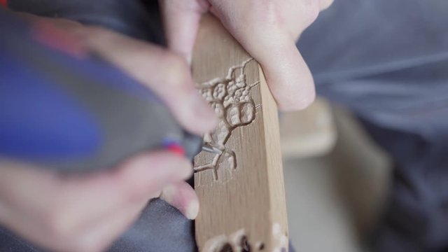 Close-up of mature craftsman using electric wood carving tool to make decoration on future chair leg