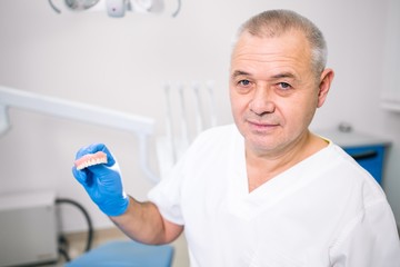 Adult male dentist holds a denture in his hand