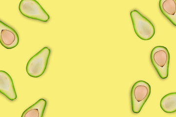 Scattered halves with and without kernels of organic avocado on yellow table in kitchen or market. Top view. Cooking concept. Copy space for your text