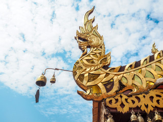 Fototapeta na wymiar Golden naga statue on roof of temple with blue sky background