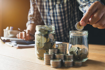 Hand putting money coin in the glass jar. Saving money, financial and accounting concept.