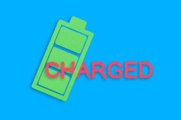Handmade paper icon of full battery with green cells near red word charged in center of blue table....