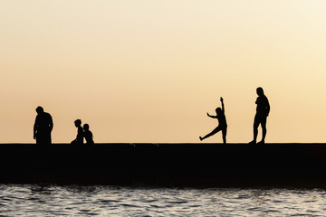 Silhouettes of people jumping from the sea pier. Rest on the sea beach