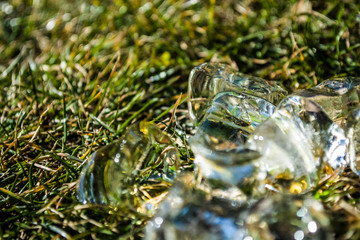 Cubes of large ice lie on a green summer grass. Play of color and patches of light. Background or texture.
